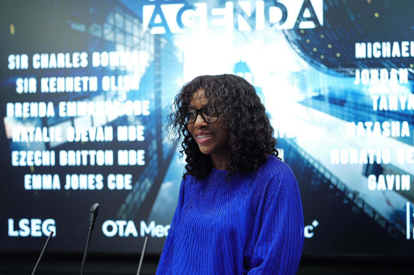 Speaker at the lectern beneath The Next Agenda screen
